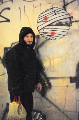 Germania, Berlino 12 2010 - artista genovese Oscar Colombo attacca personaggio ferito disegnato su carta con la colla sul muro - personaggi feriti che si curano progressivamente, appiccicati ai muri dell'inverno berlinese