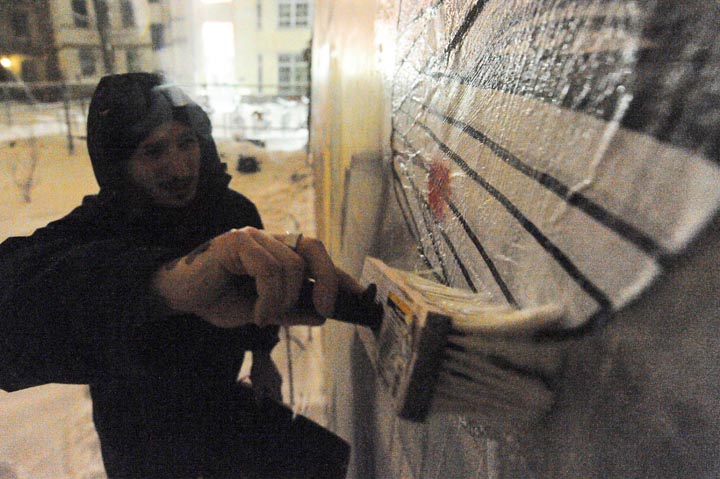 Germania, Berlino 12 2010 - artista genovese Oscar Colombo attacca personaggio ferito disegnato su carta con la colla sul muro - personaggi feriti che si curano progressivamente, appiccicati ai muri dell'inverno berlinese